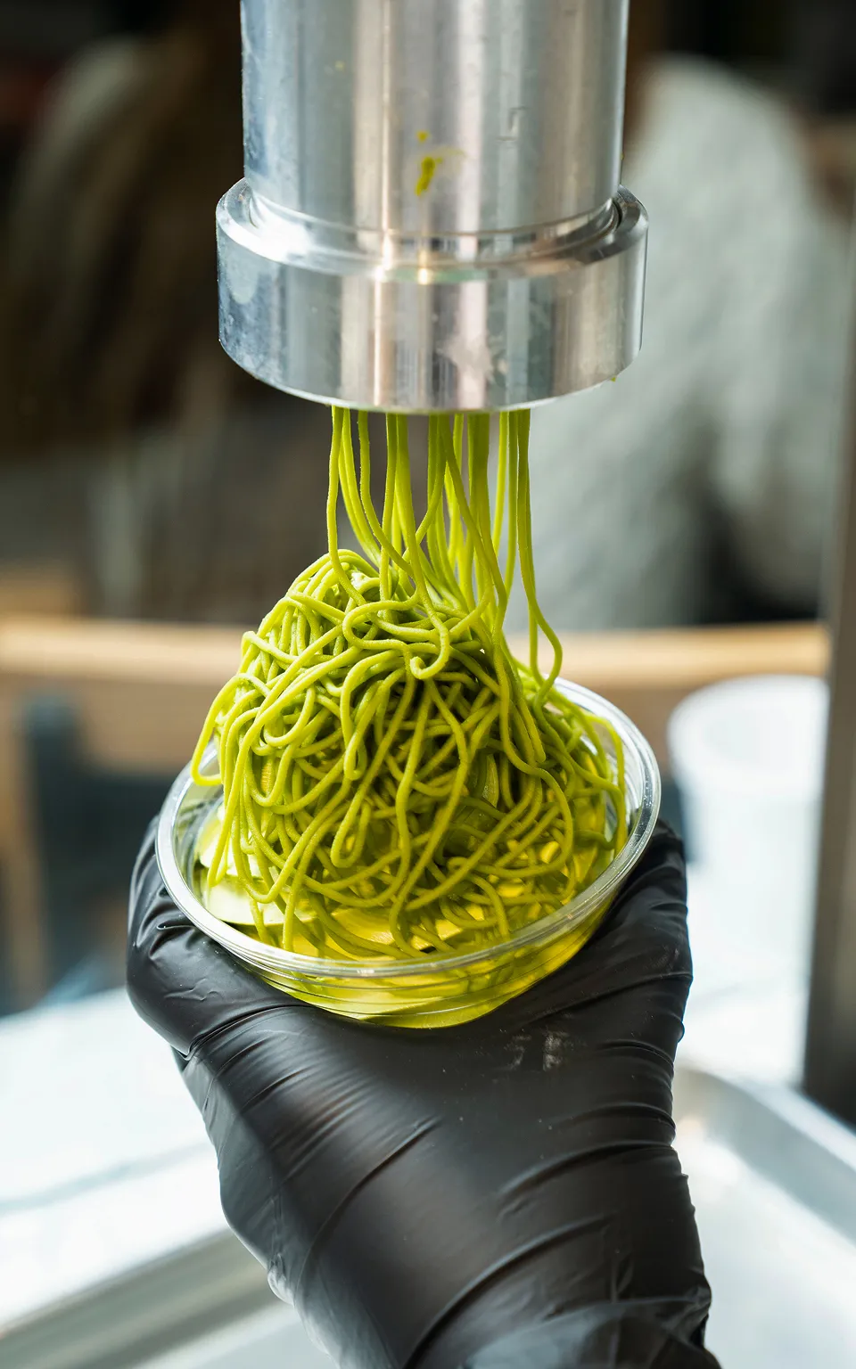 Matcha sauce flows down from a special extruder into a transparent cup. The cup is held in the hand and receives the matcha topping in the form of sauce on top of the matcha cream. Matcha dessert serving process.